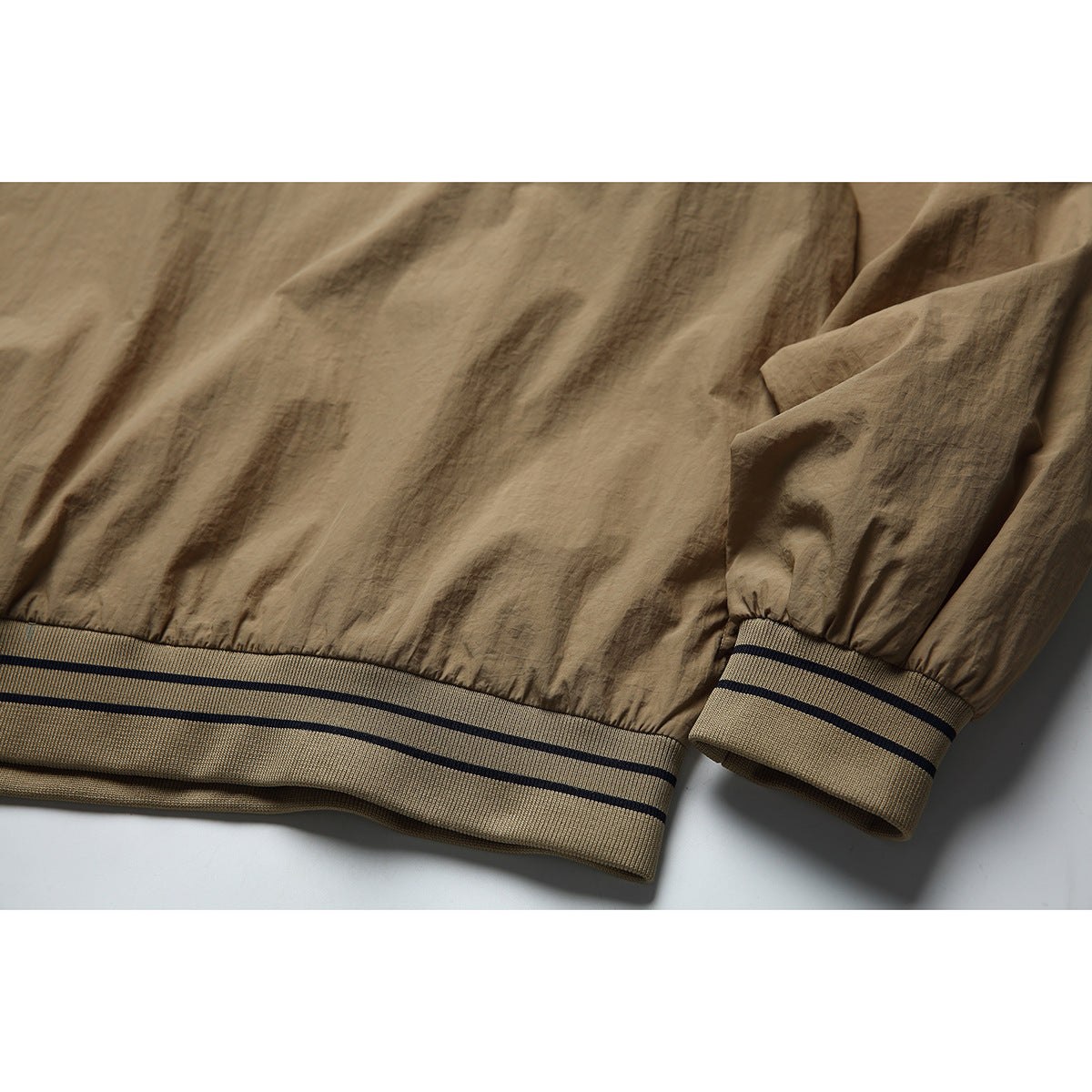 Close-up of the tan jacket's elastic hem and sleeve cuff, both finished with striped ribbed trim.