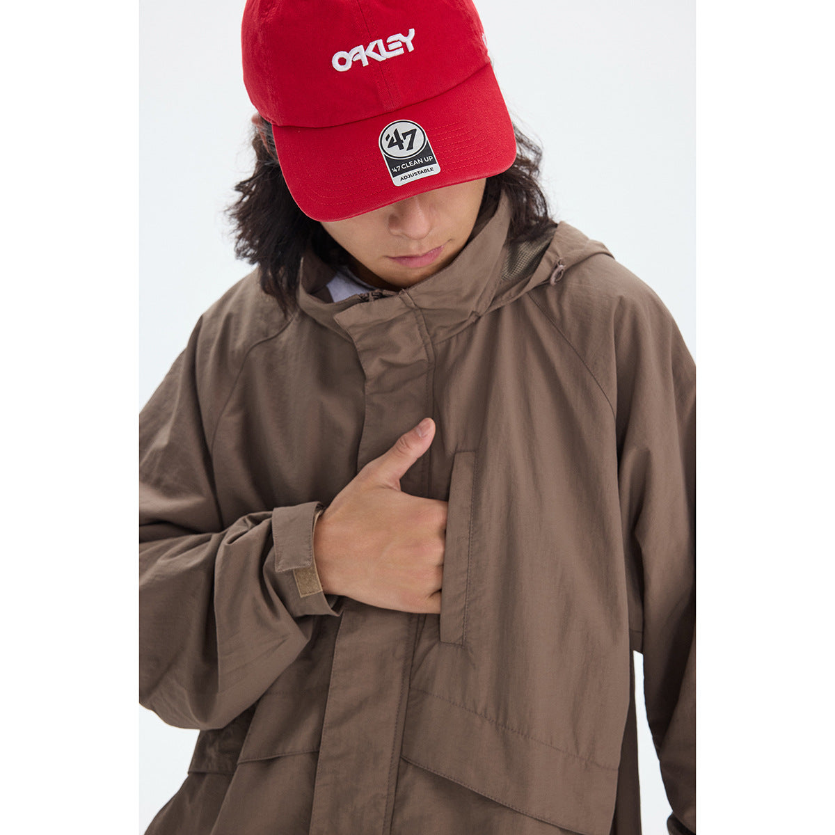 Close-up of a taupe hooded jacket's front closure and sleeve, worn with a red cap.