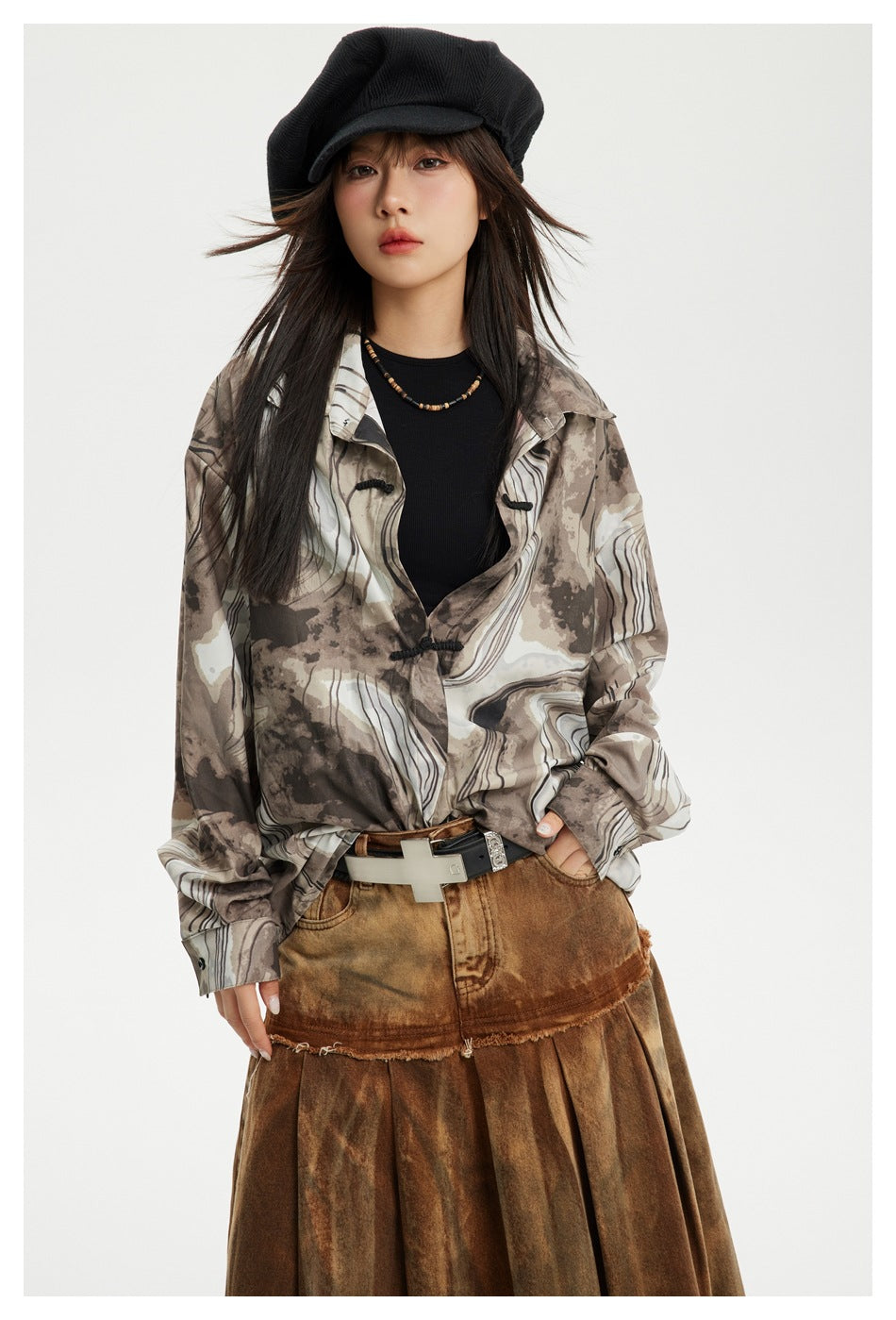 Front view of a model wearing a taupe and cream abstract-print shirt with black frog closures.