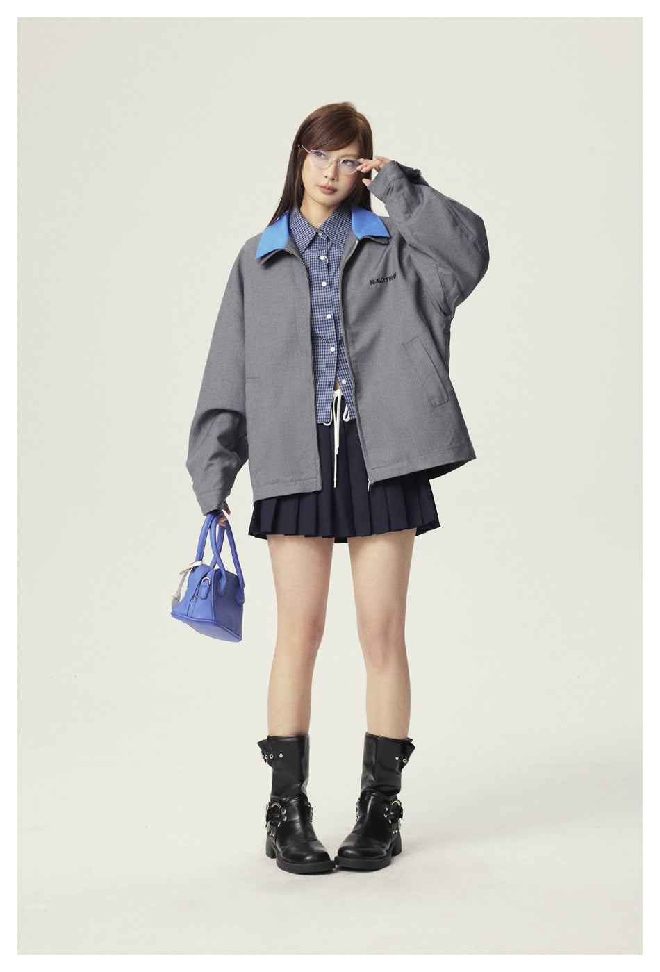 Model wearing a charcoal-gray jacket with a bright blue collar over a checked shirt and pleated navy skirt.