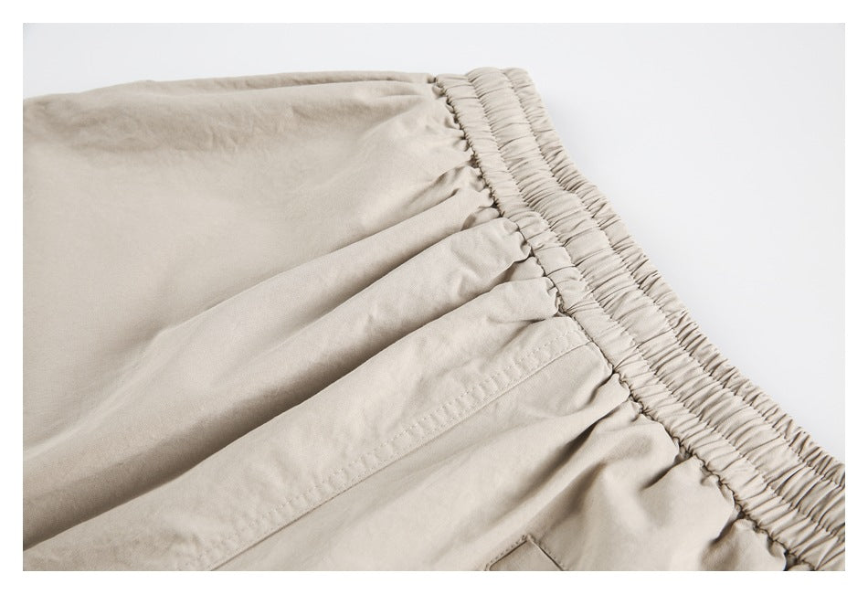 Close-up of beige trousers showing a gathered elastic waistband and stitched pocket seam.