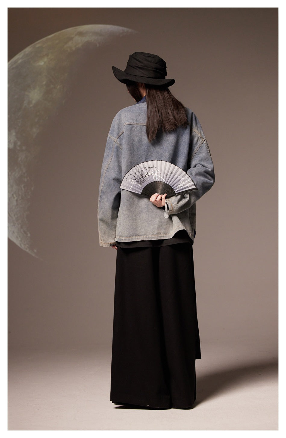 Back view of a model wearing a loose gray denim jacket with a plain back and a long black skirt.
