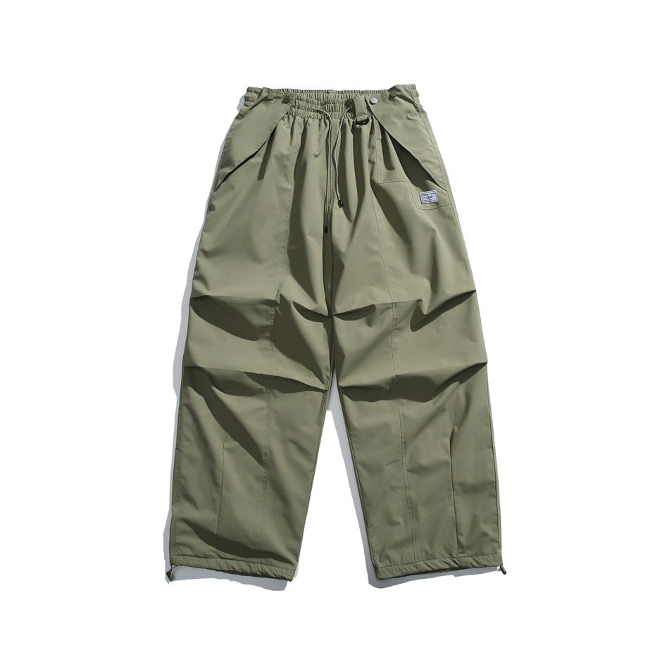 Front view of olive khaki wide-leg pants with an elastic drawstring waist, angled pockets, knee panels and ankle toggles.