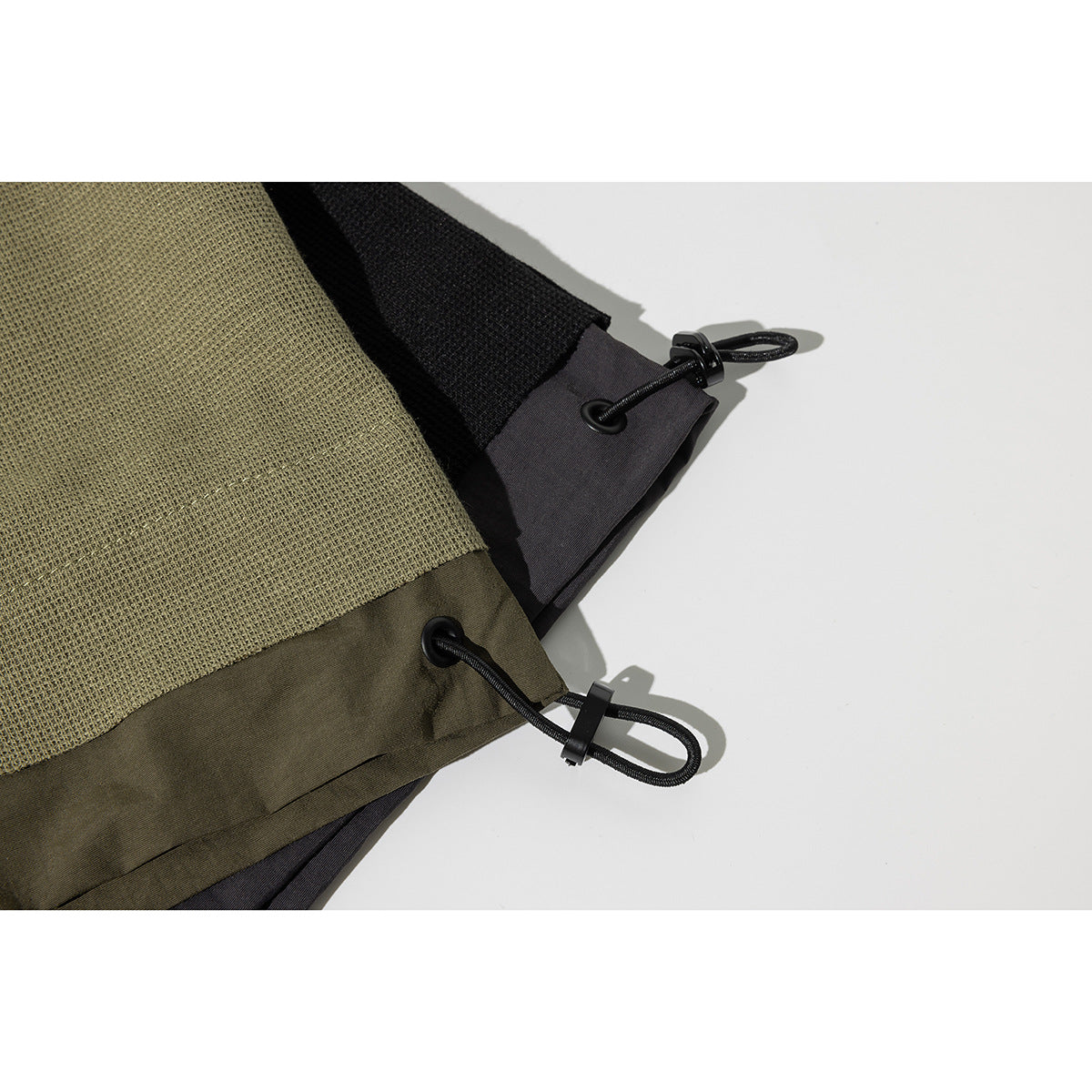 Close-up of olive and black T-shirt hems with black elastic cord loops and toggles.