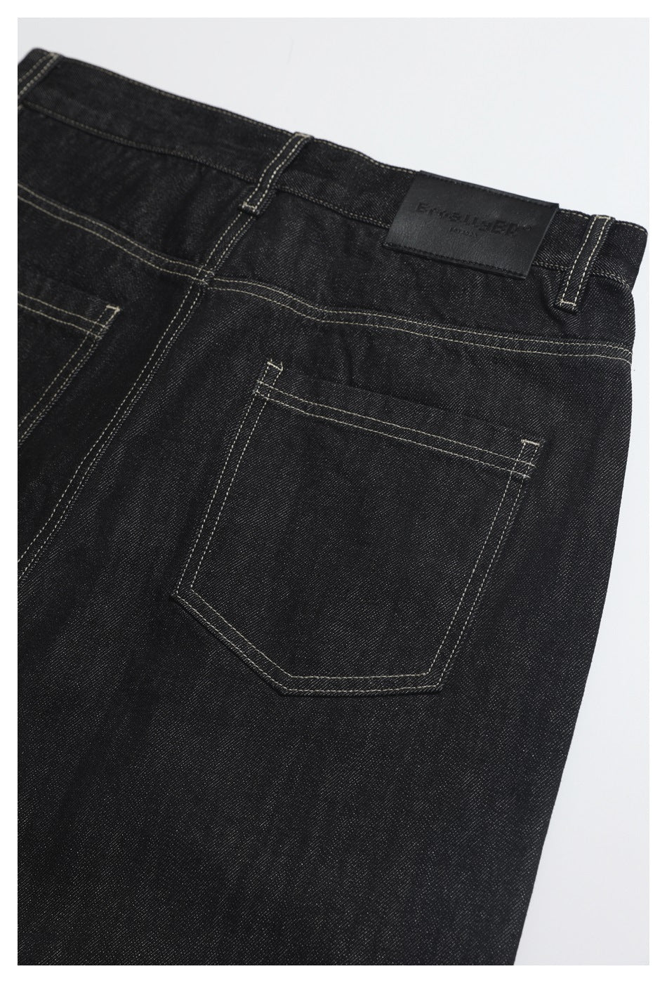 Close view of the back of black jeans, showing a stitched pocket, belt loops and waistband patch.