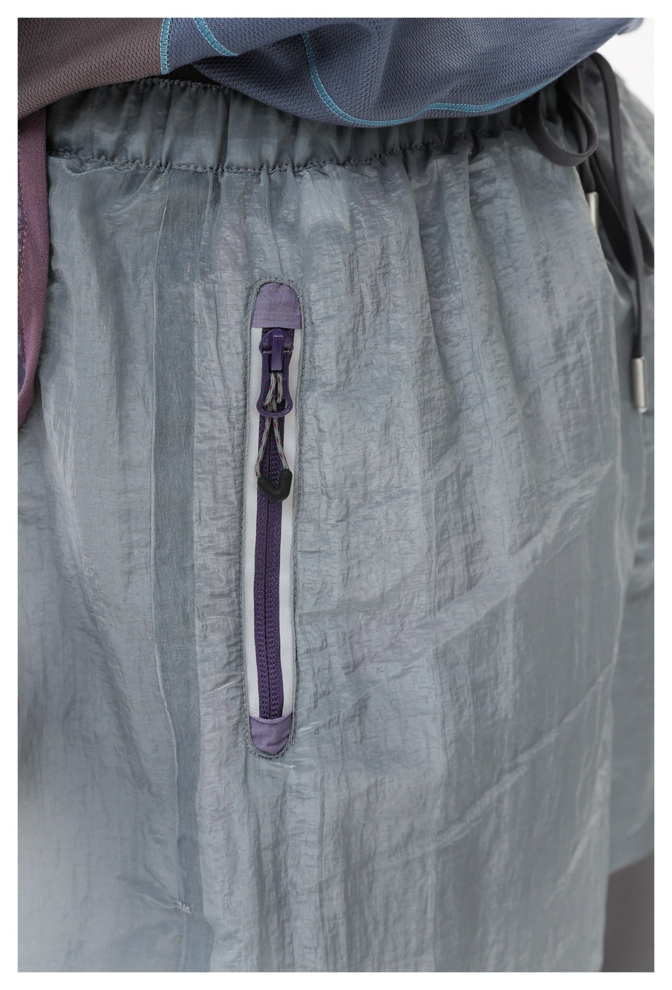 Close-up of the pale blue-gray shorts' elastic waistband and vertical purple zip pocket.