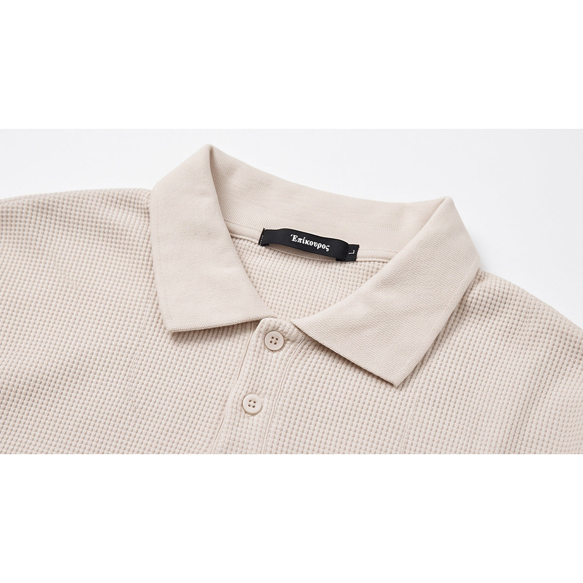 Close-up of a cream textured polo shirt collar, two buttons, and black neck label.