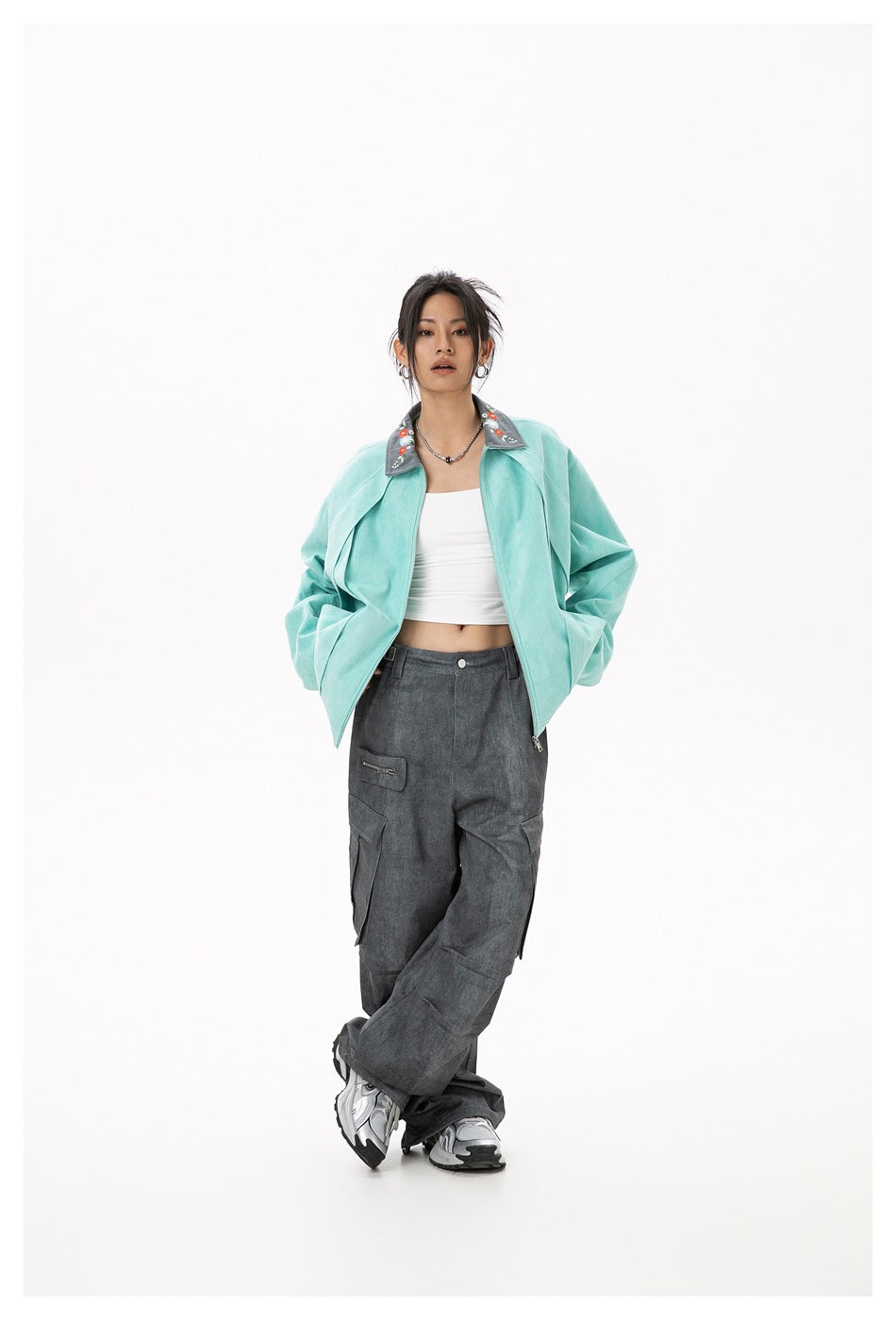 Model wearing open light green jacket with embroidered collar over white crop top and gray cargo pants, hands in pockets