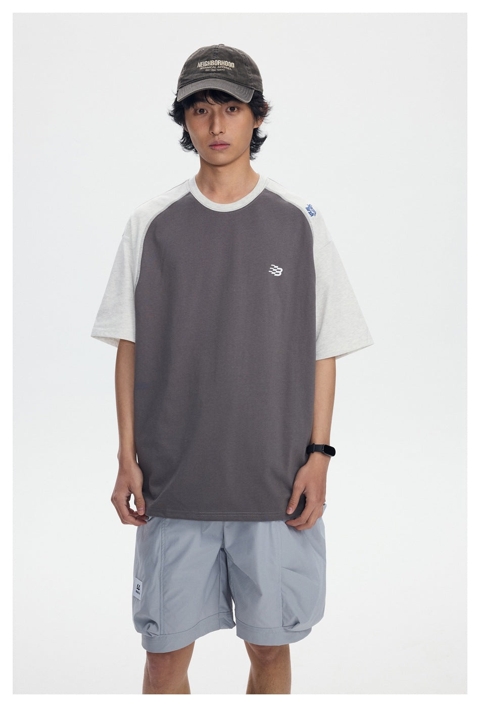 Front view of a model wearing a charcoal T-shirt with light gray raglan sleeves and a small chest emblem.