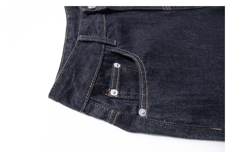 Close-up of dark indigo jeans showing the front pocket, coin pocket, and metal rivets.