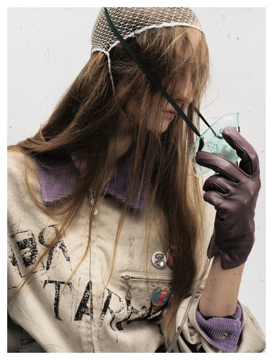 Close-up front view of a model wearing a distressed beige jacket with a purple collar, graphic print, and pins.