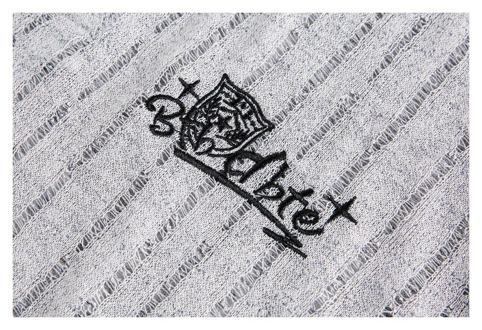 Close-up of a black embroidered crest and lettering on gray fabric with openwork stripe details.
