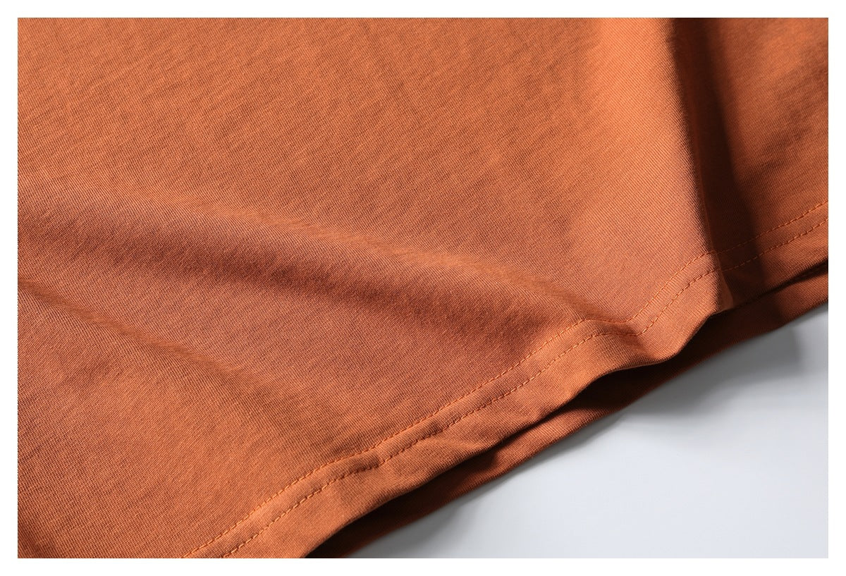 Close-up of the double-stitched hem on rust-orange T-shirt fabric.