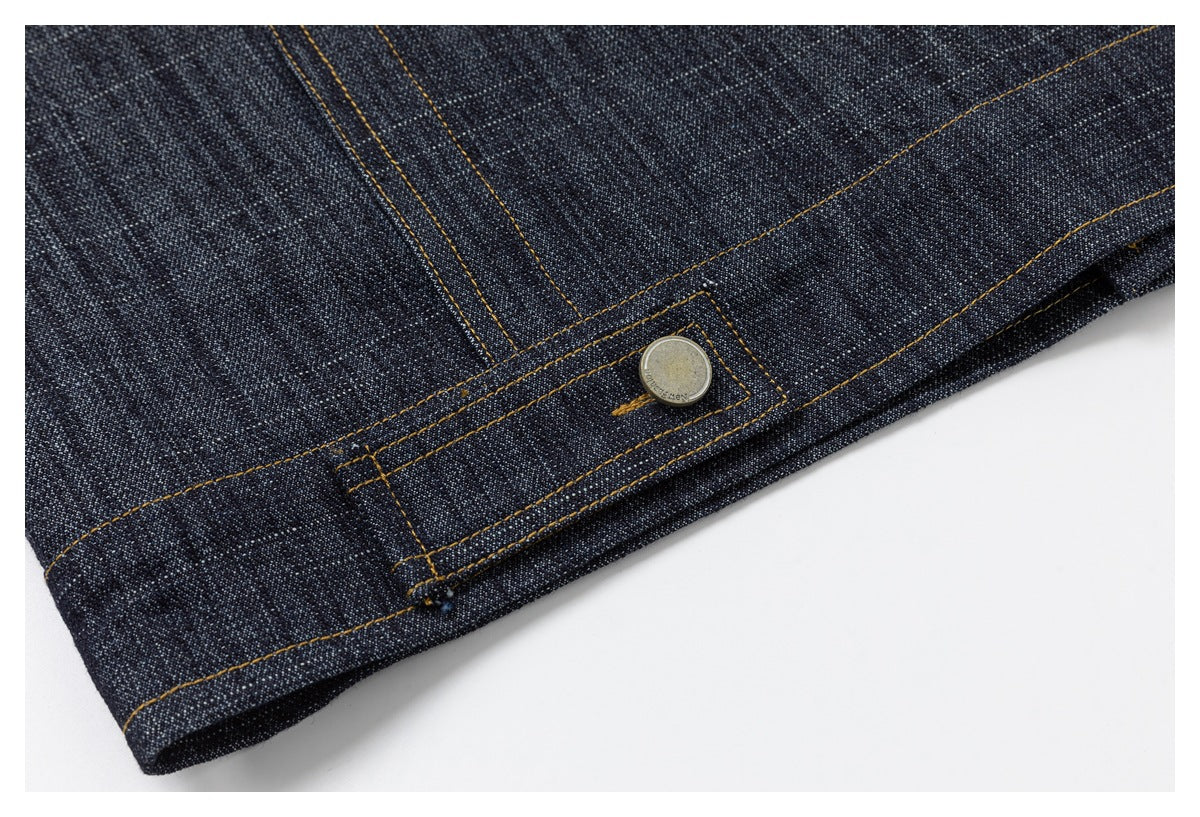 Close-up of a stitched adjustment tab with a metal button on dark indigo denim.