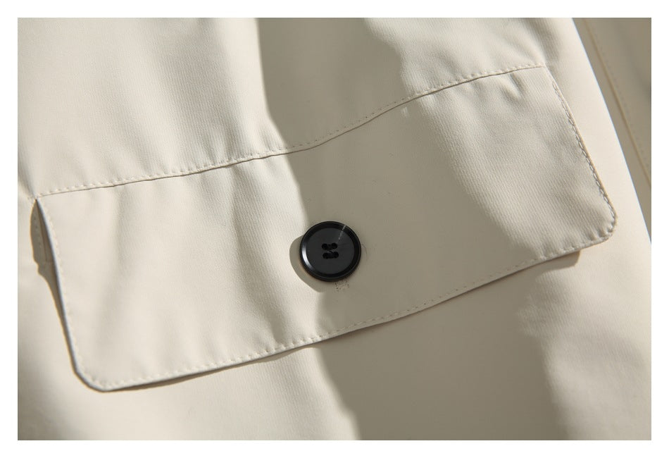 Close-up of an ivory coat's large flap pocket with a dark button.