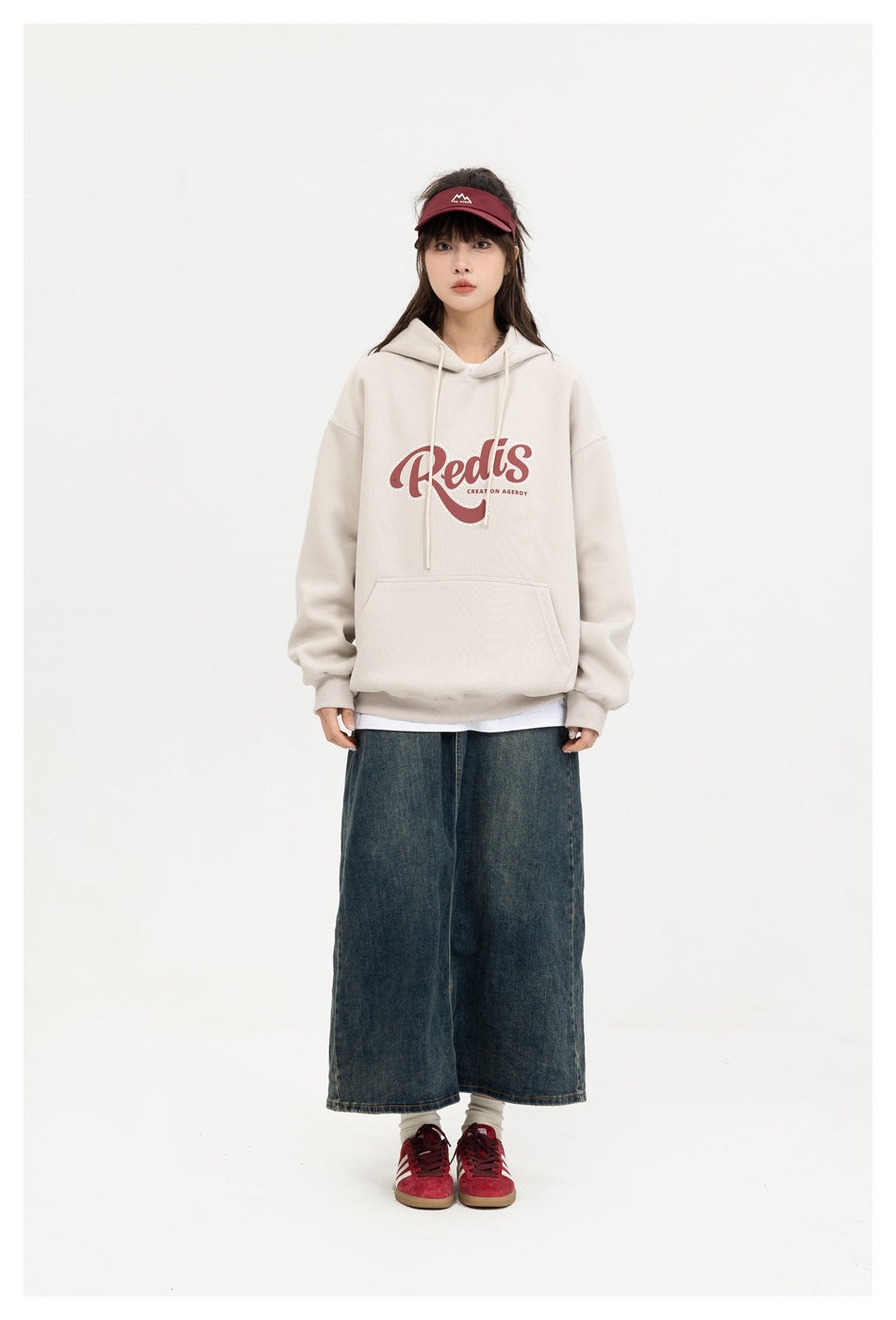 Full-length view of a model wearing a cream graphic hoodie with a long denim skirt and red visor.