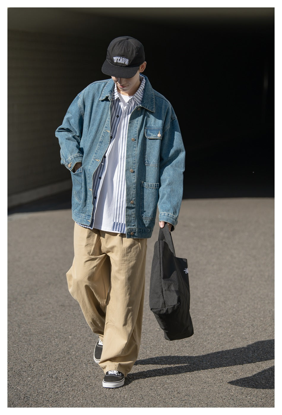 Model wearing an oversized blue denim jacket with flap pockets, layered over a striped shirt and white tee.