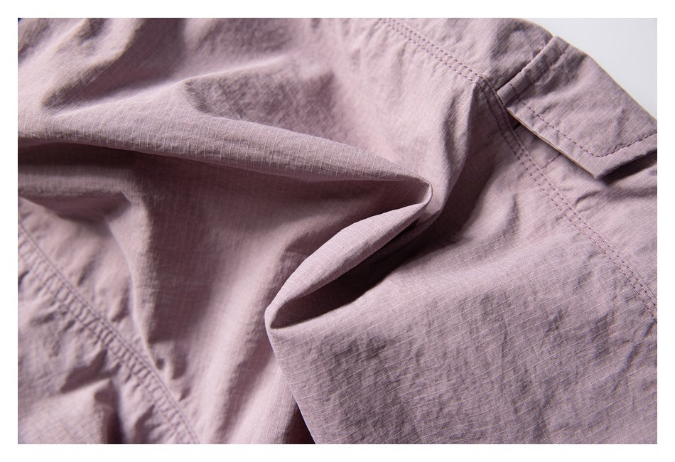 Close-up of dusty mauve garment showing a folded fabric edge, fine grid texture and stitched pocket detail.
