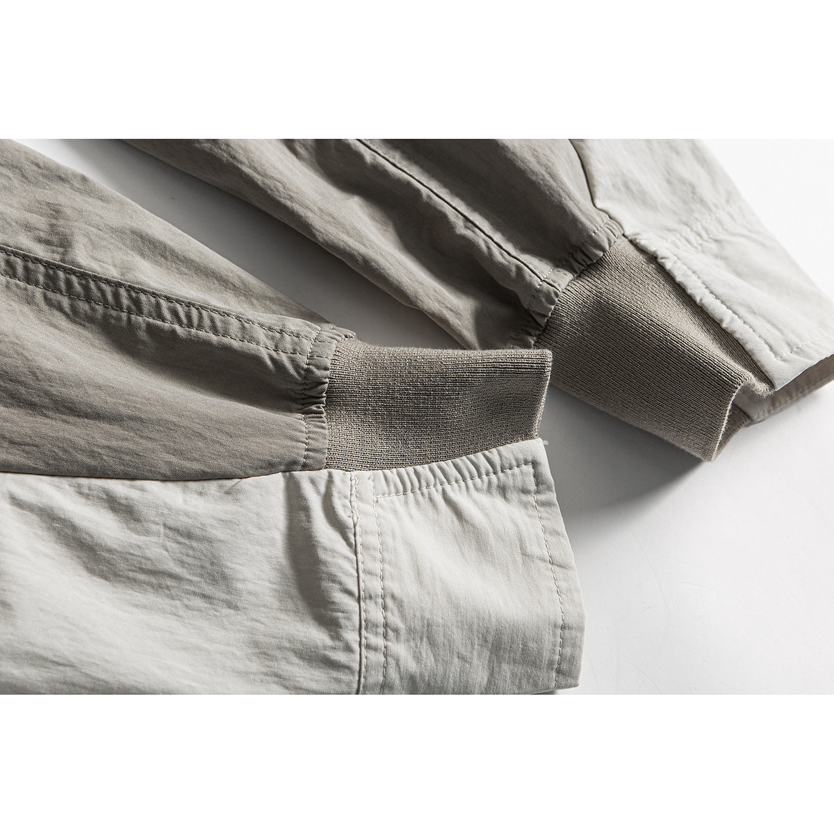 Close-up of light gray shirt sleeves with ribbed cuffs and a section of the lower hem.
