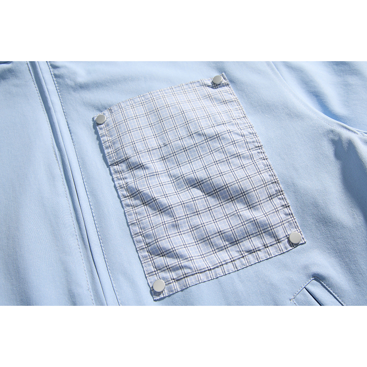 Close-up of a light blue jacket's plaid chest pocket, secured with four round snaps.