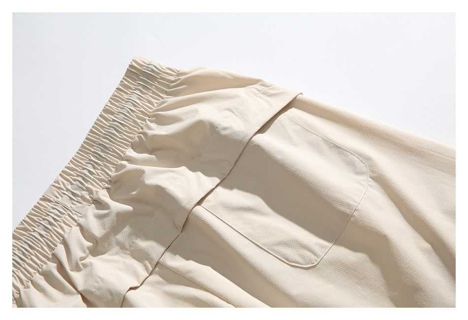 Close-up of the gathered waistband and curved patch pocket on cream pants.