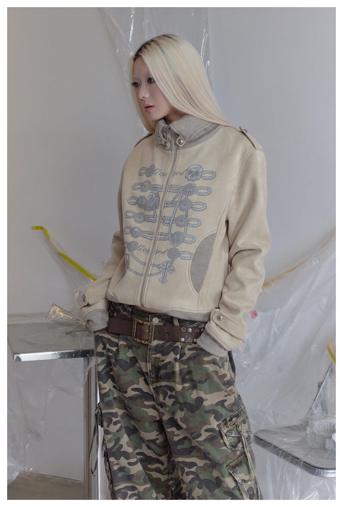 Close three-quarter view of a model in the beige jacket with gray braided cord graphic, ribbed collar and camo pants