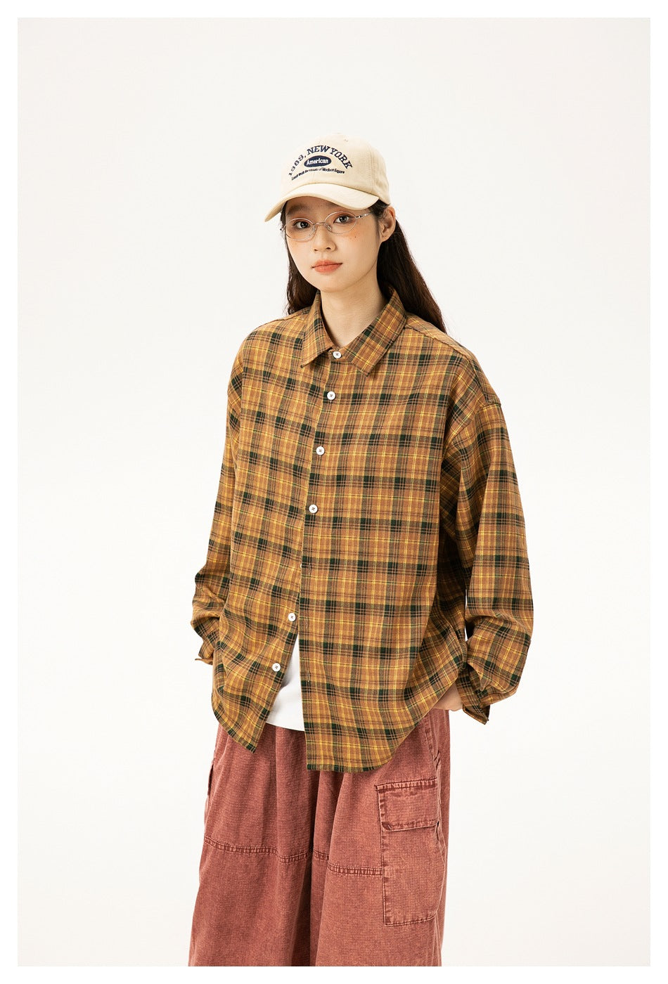 Model wearing an oversized mustard and dark plaid button-up shirt with rust cargo pants and a beige cap.