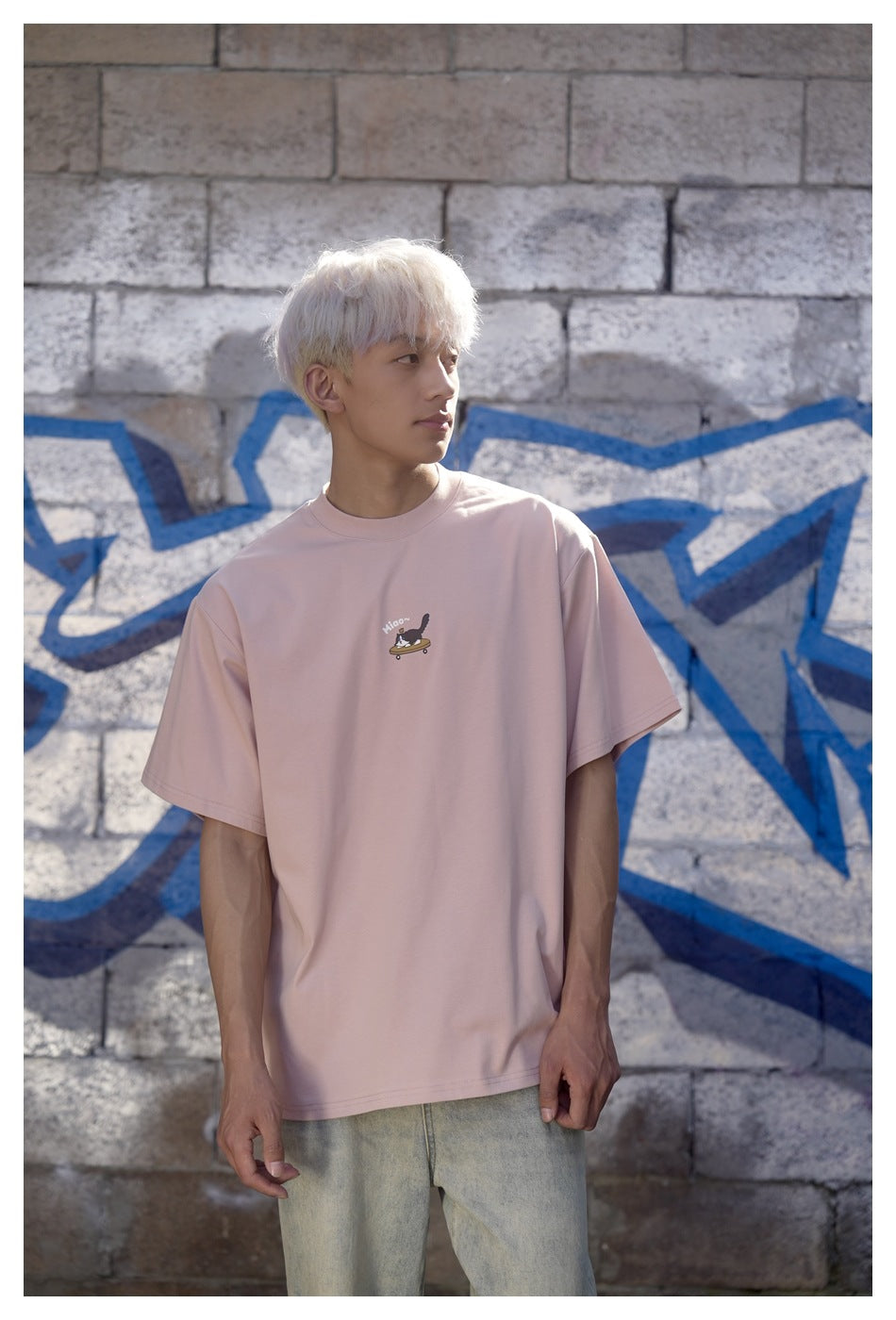 Model wearing a pale pink oversized T-shirt with a small cat-on-skateboard chest graphic, shown from the front.