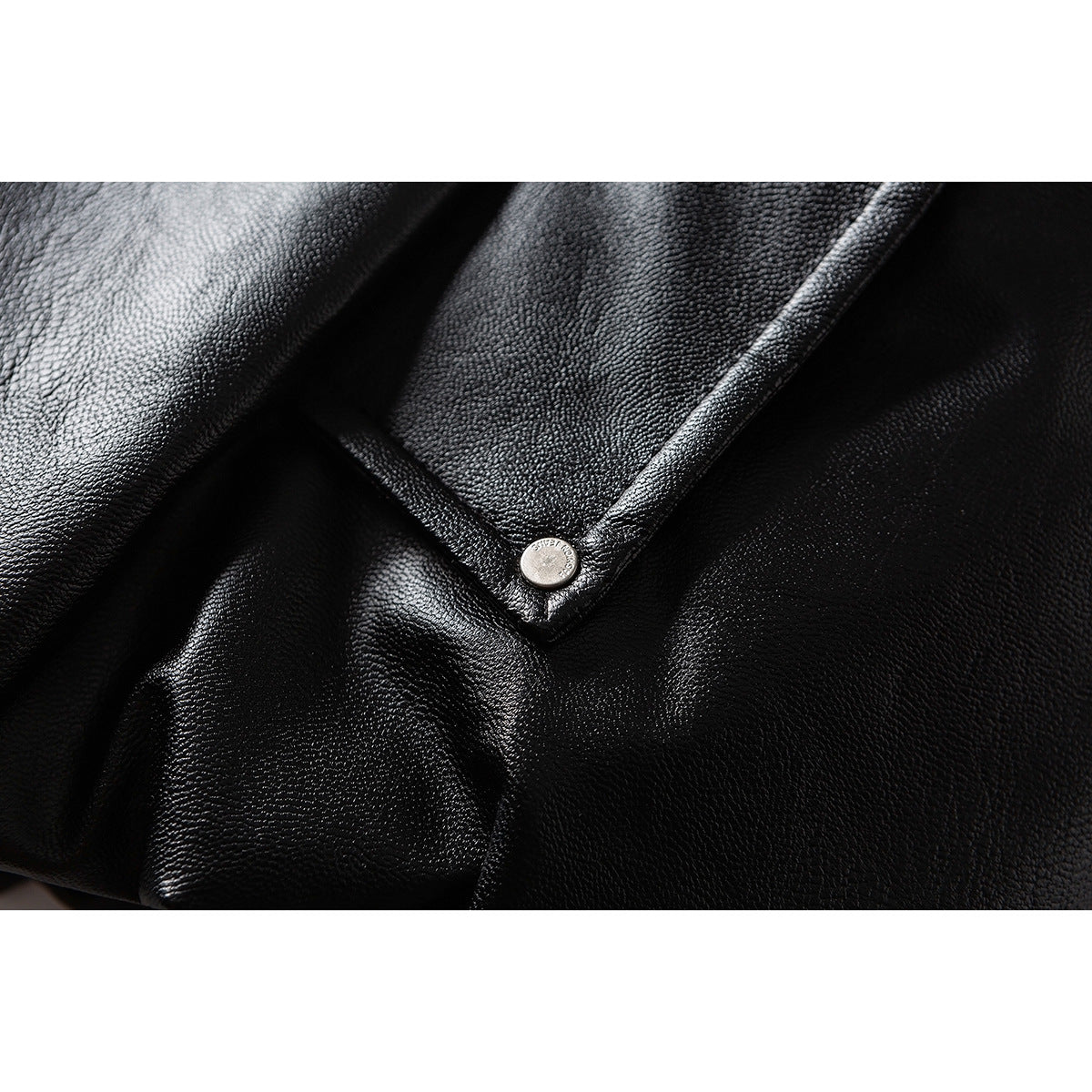 Close-up of a black jacket's pebbled surface, stitched flap, and silver snap button.