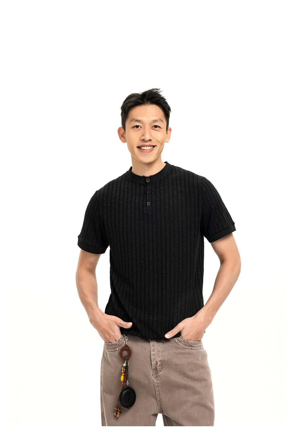 Man wearing a black ribbed knit short-sleeve henley top with three buttons, hands in pockets of brown jeans