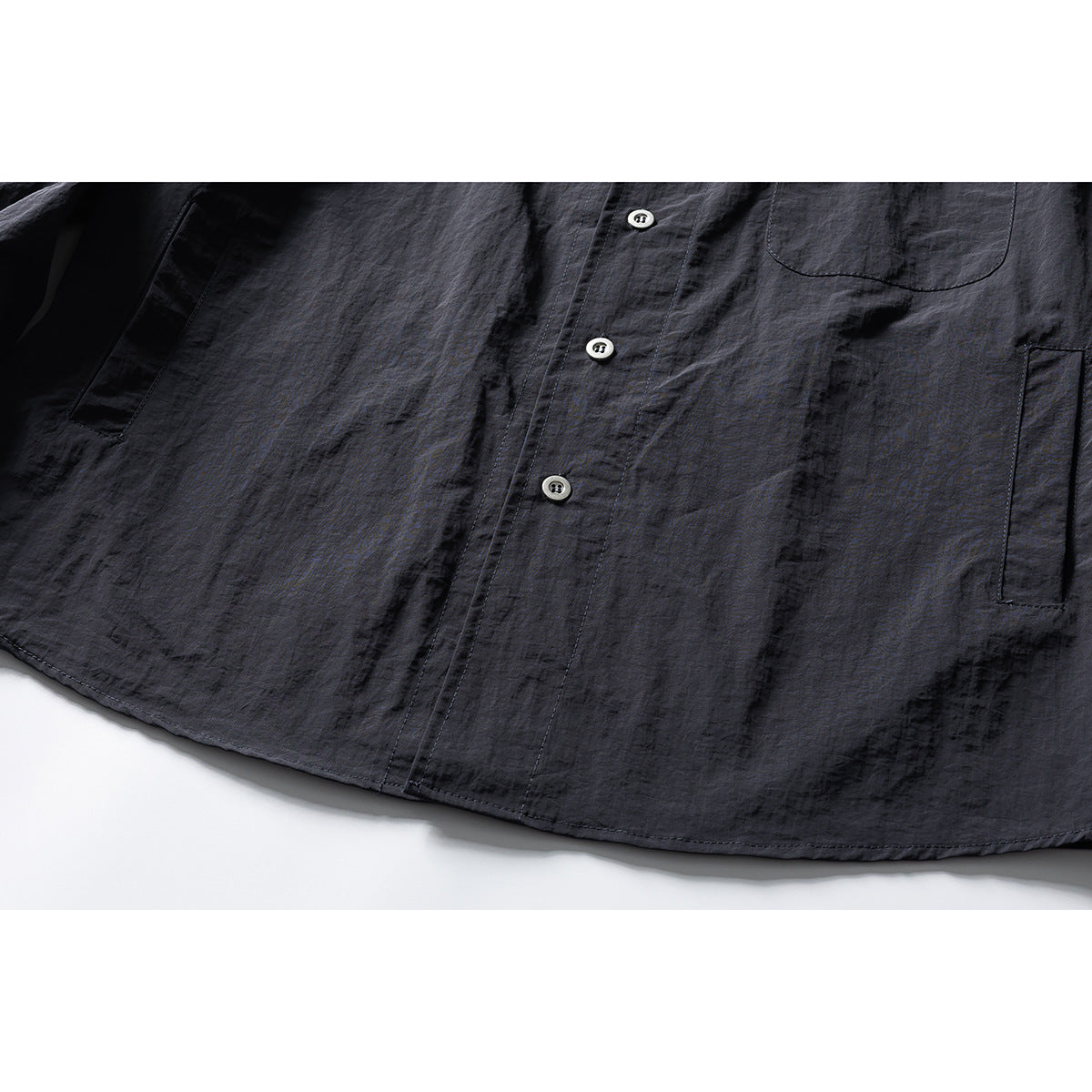 Close-up of a dark charcoal shirt front showing its button placket, chest pocket, and lower side pockets.