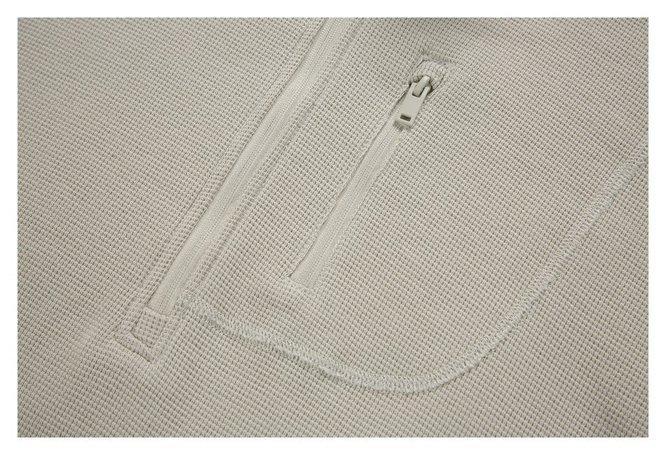 Close-up of the light beige pullover's vertical zip pocket and textured fabric.