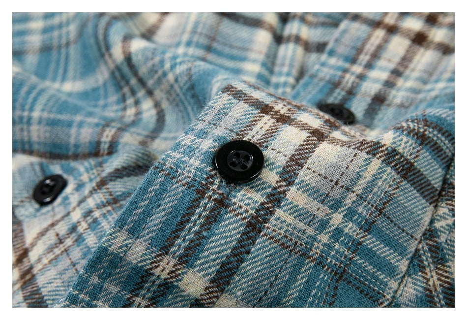 Close-up of black buttons and plaid fabric on a blue, cream, and brown shirt.