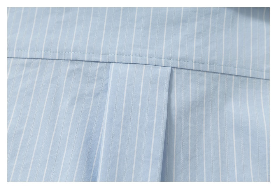 Close-up of light blue pinstriped fabric showing a horizontal seam and a central pleat.