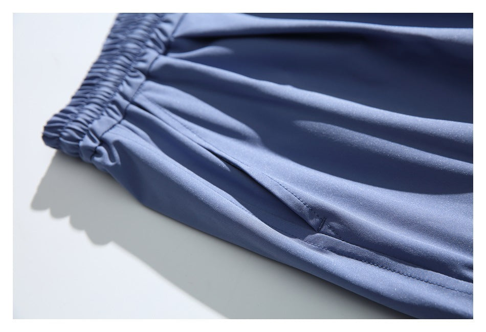 Close-up of slate blue pants showing the elastic waistband, fabric folds and a stitched pocket opening.