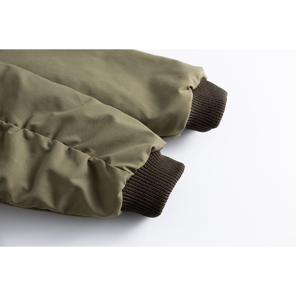 Close-up of olive jacket sleeves ending in dark brown ribbed cuffs.