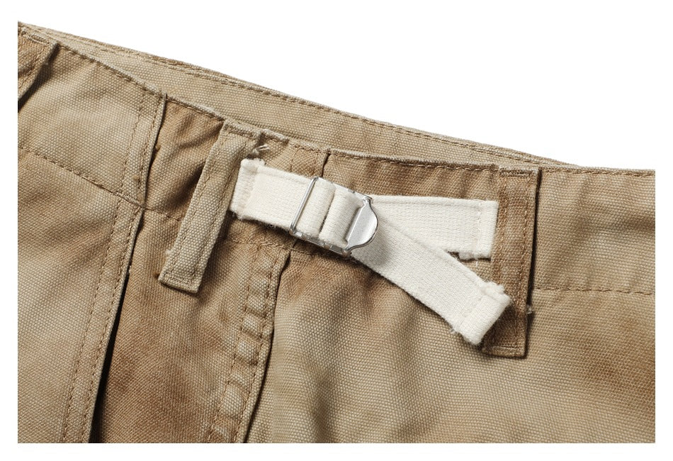 Close-up of tan shorts waistband with a white adjustable strap and metal buckle.