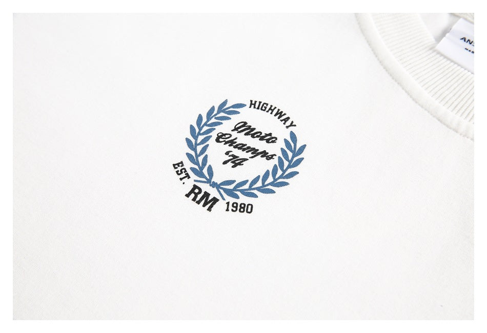 Close-up of a white sweatshirt chest with a blue laurel-wreath graphic and English lettering beside the ribbed neckline.