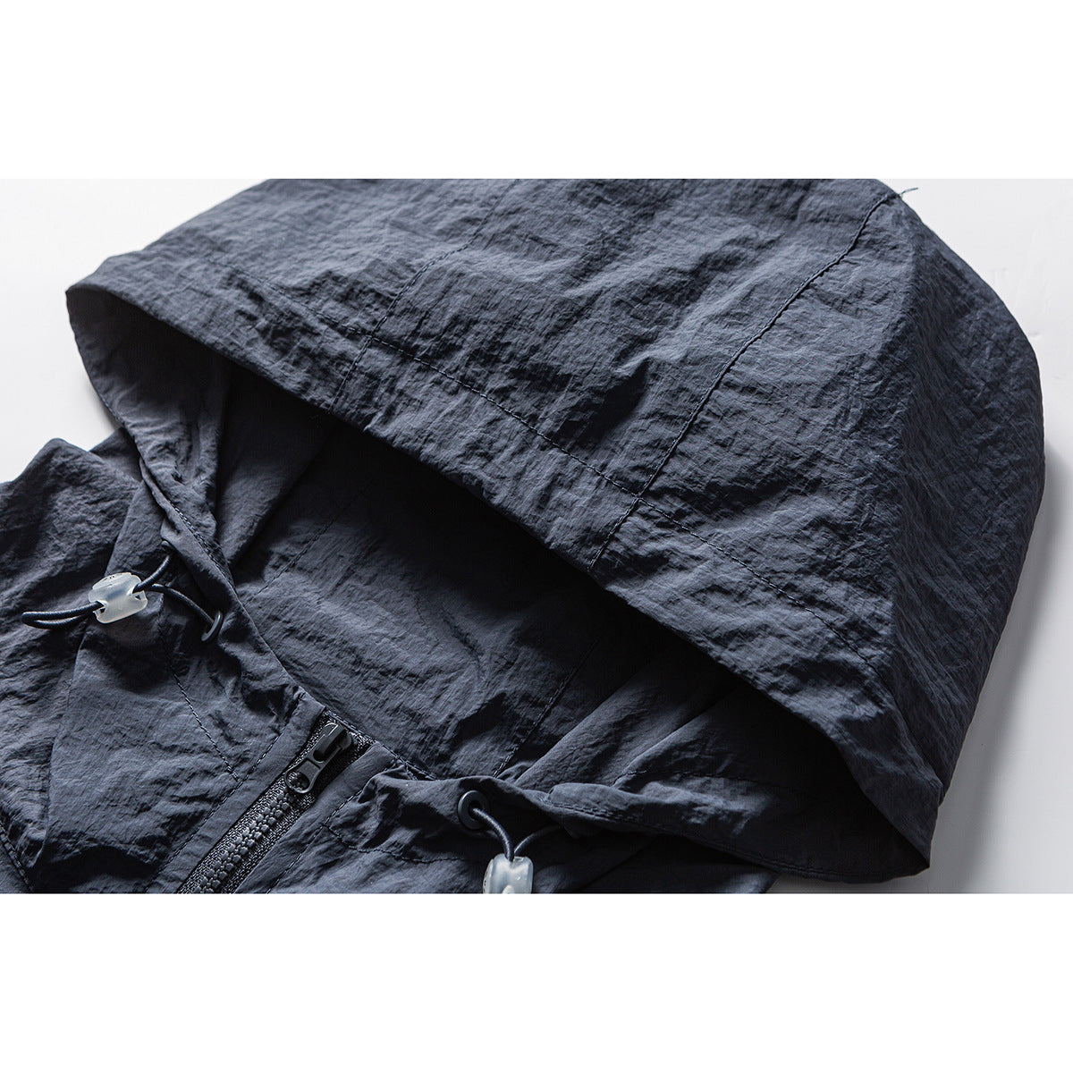 Close-up of a charcoal hooded jacket showing its hood, drawcord toggles and front zipper.