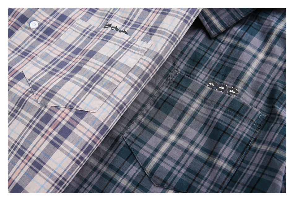 Two plaid button-up shirts in pale blush and blue-gray and dark teal, shown with chest pockets and small cat motifs.