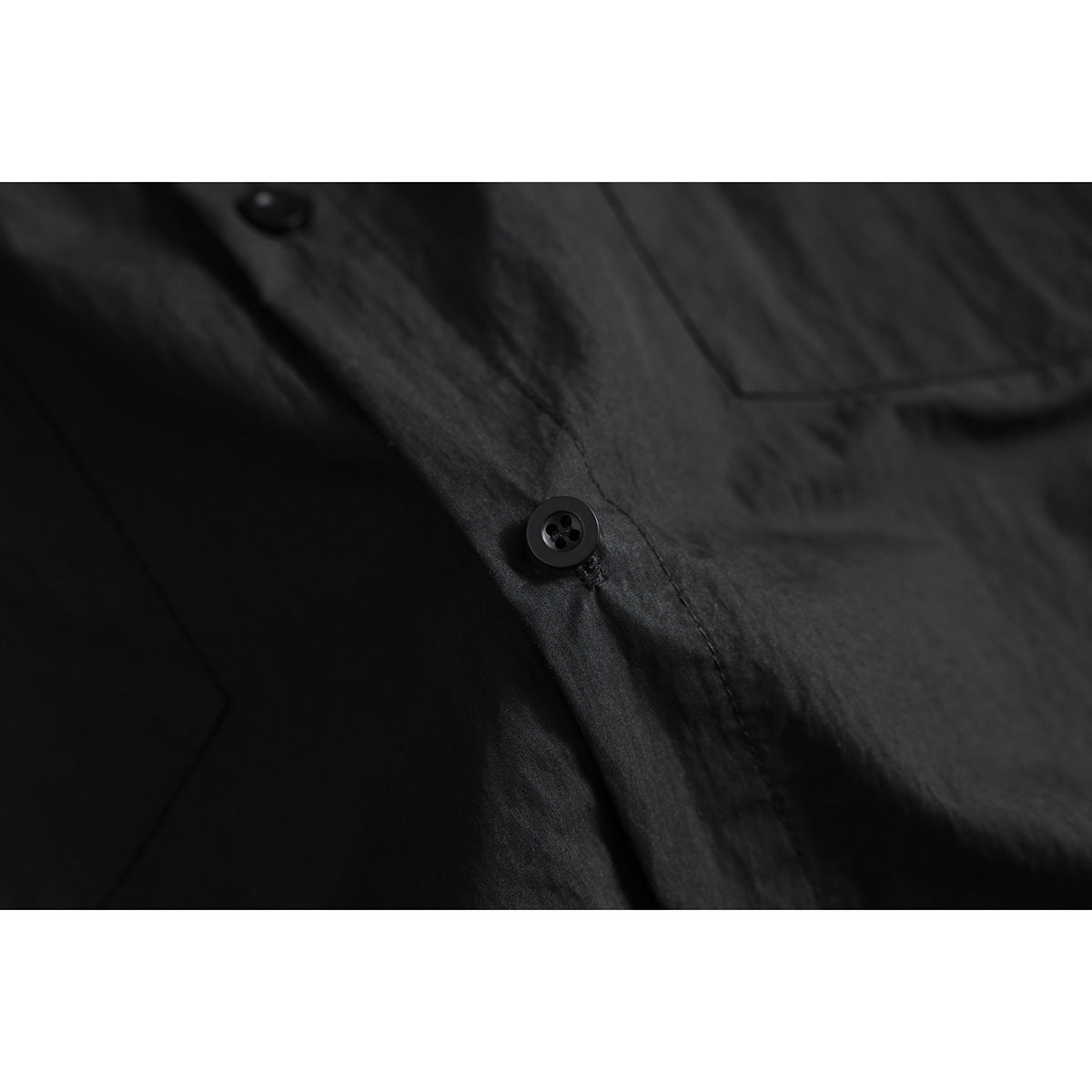 Close-up of a black shirt's button placket, button, and chest pocket seam.