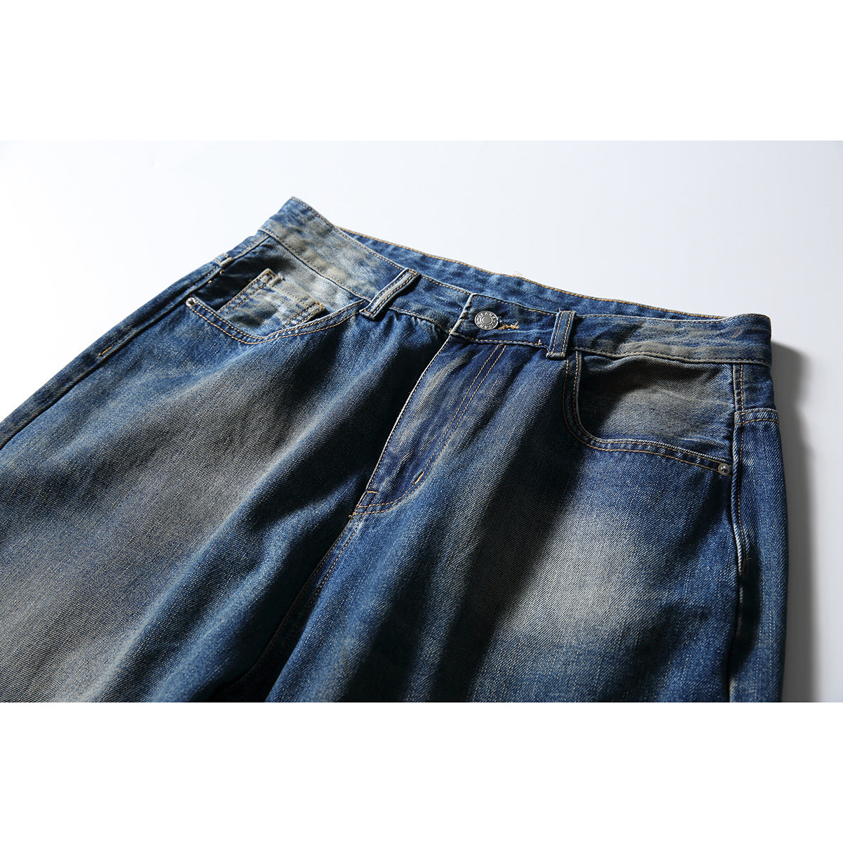 Close-up of the front waist and pockets of blue faded jeans with contrast stitching and a metal button.