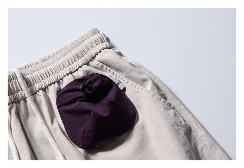Close-up of a dark plum pocket with a black cord toggle on light beige shorts.