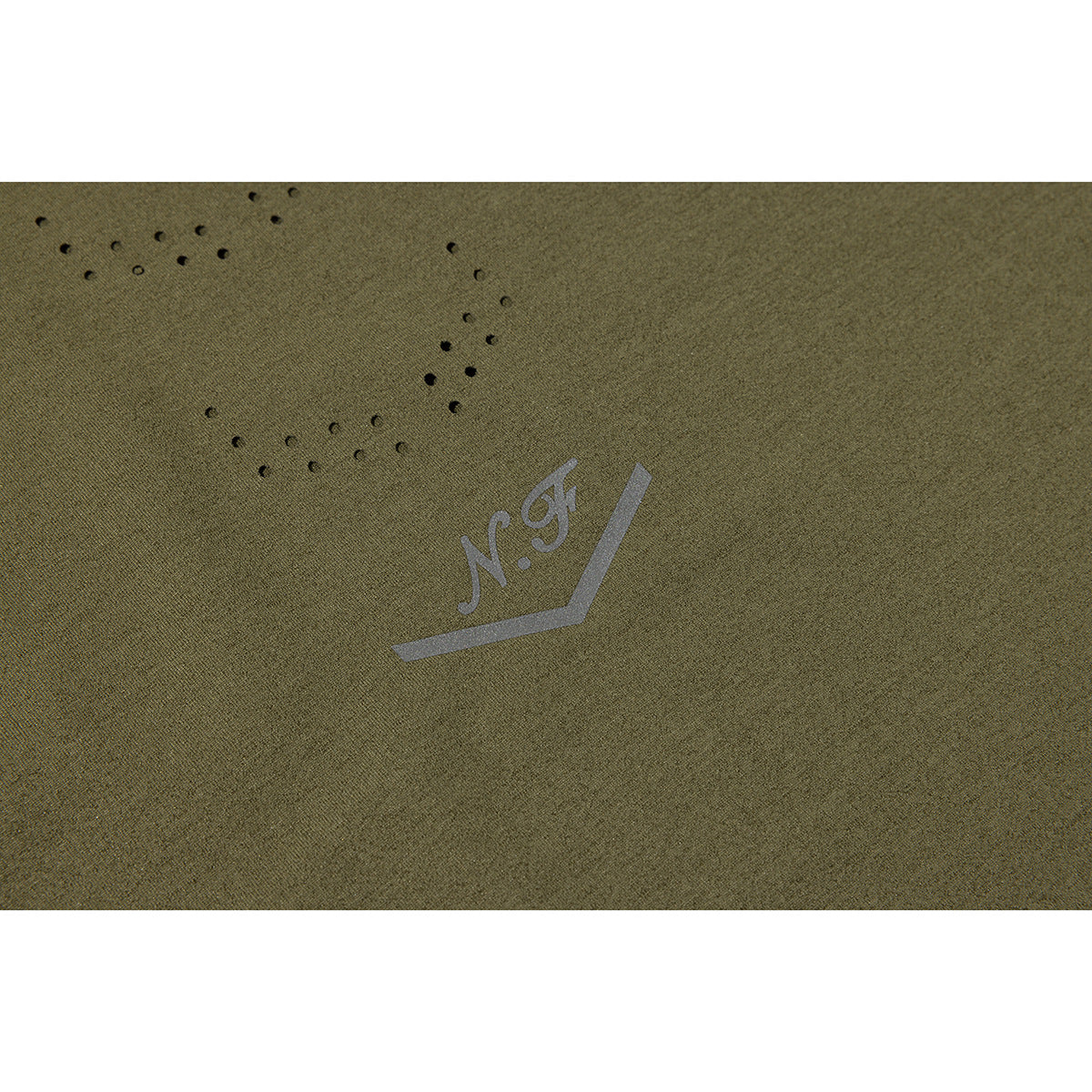 Close-up of olive-green T-shirt fabric with a small gray emblem and decorative perforations.