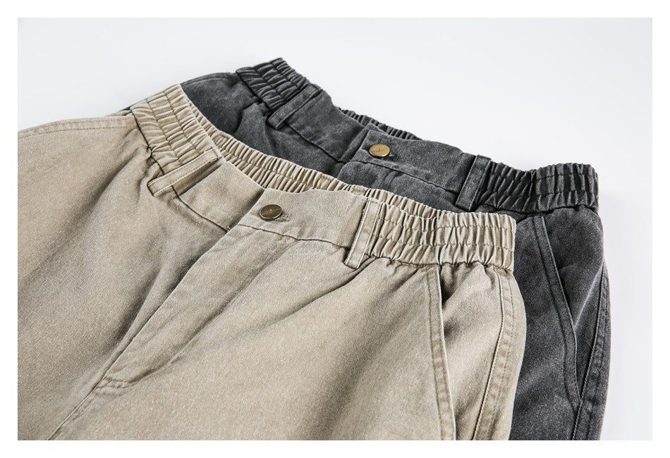 Angled close-up of light beige and charcoal cargo pants showing their elasticized waistbands, buttons, and belt loops.