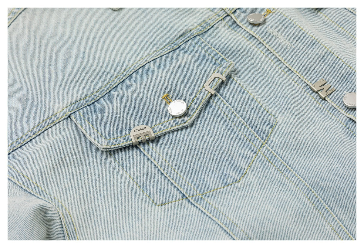 Close-up of a pale blue denim jacket pocket with yellow stitching and silver-tone decorative hardware.