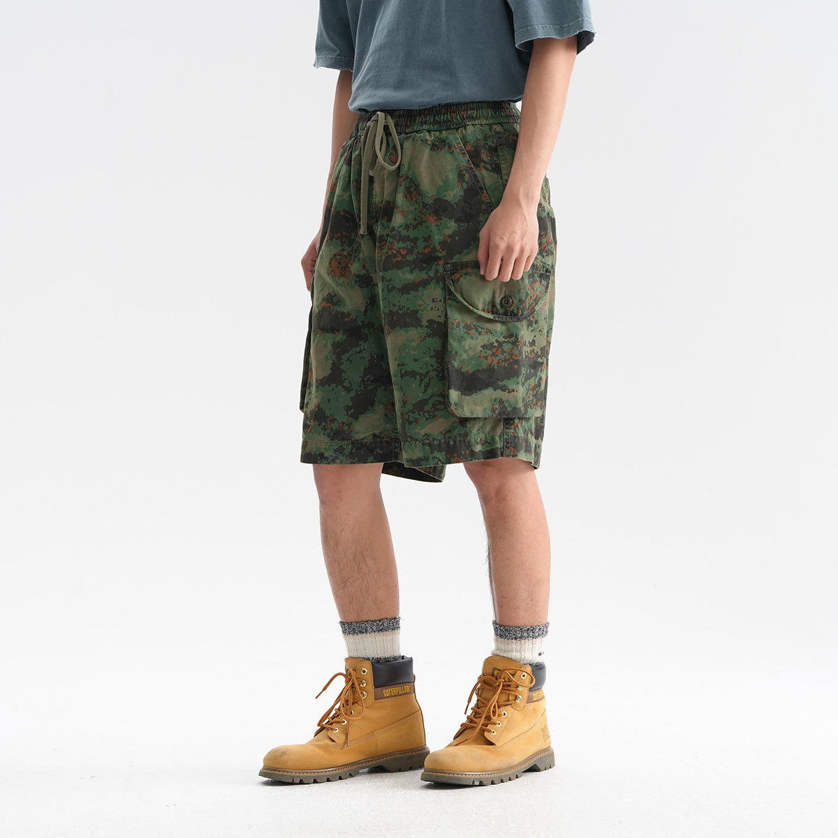 Angled front view of a model wearing green camouflage cargo shorts with a drawstring waist and large flap pocket.