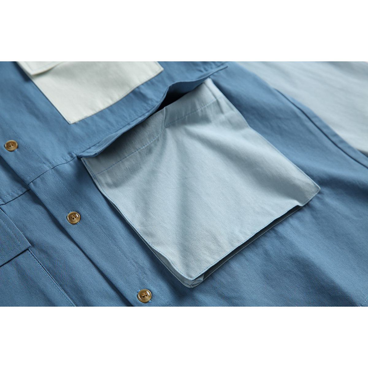 Close-up of a large pale blue flap pocket and brown buttons on a blue color-block shirt.
