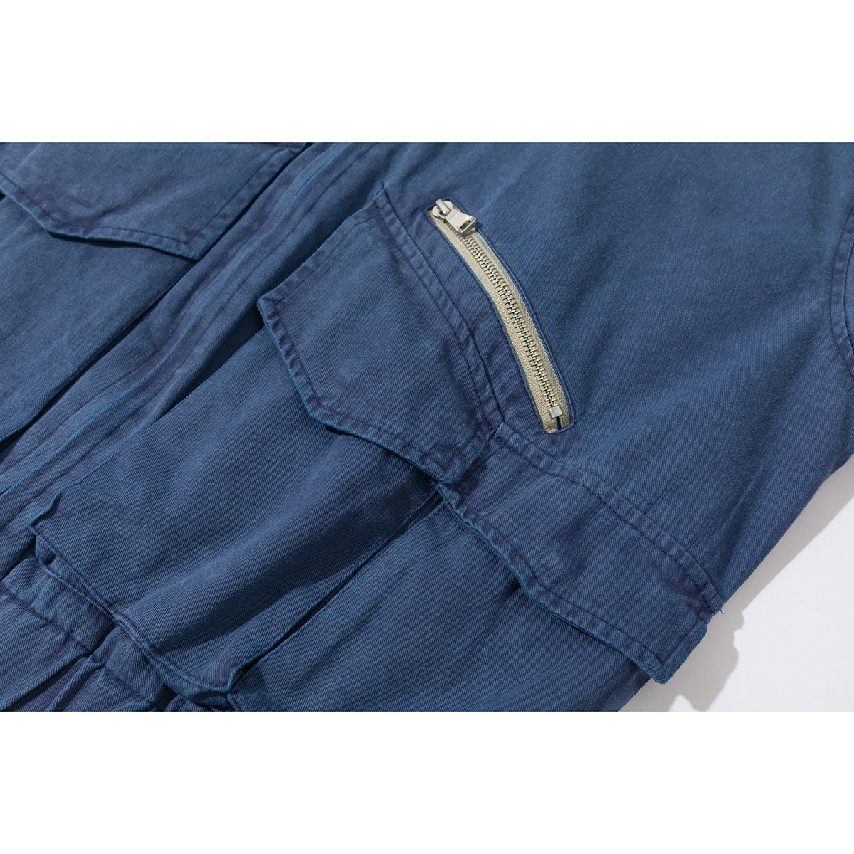 Close-up of a blue jacket's flap pocket and angled metal zipper pocket.