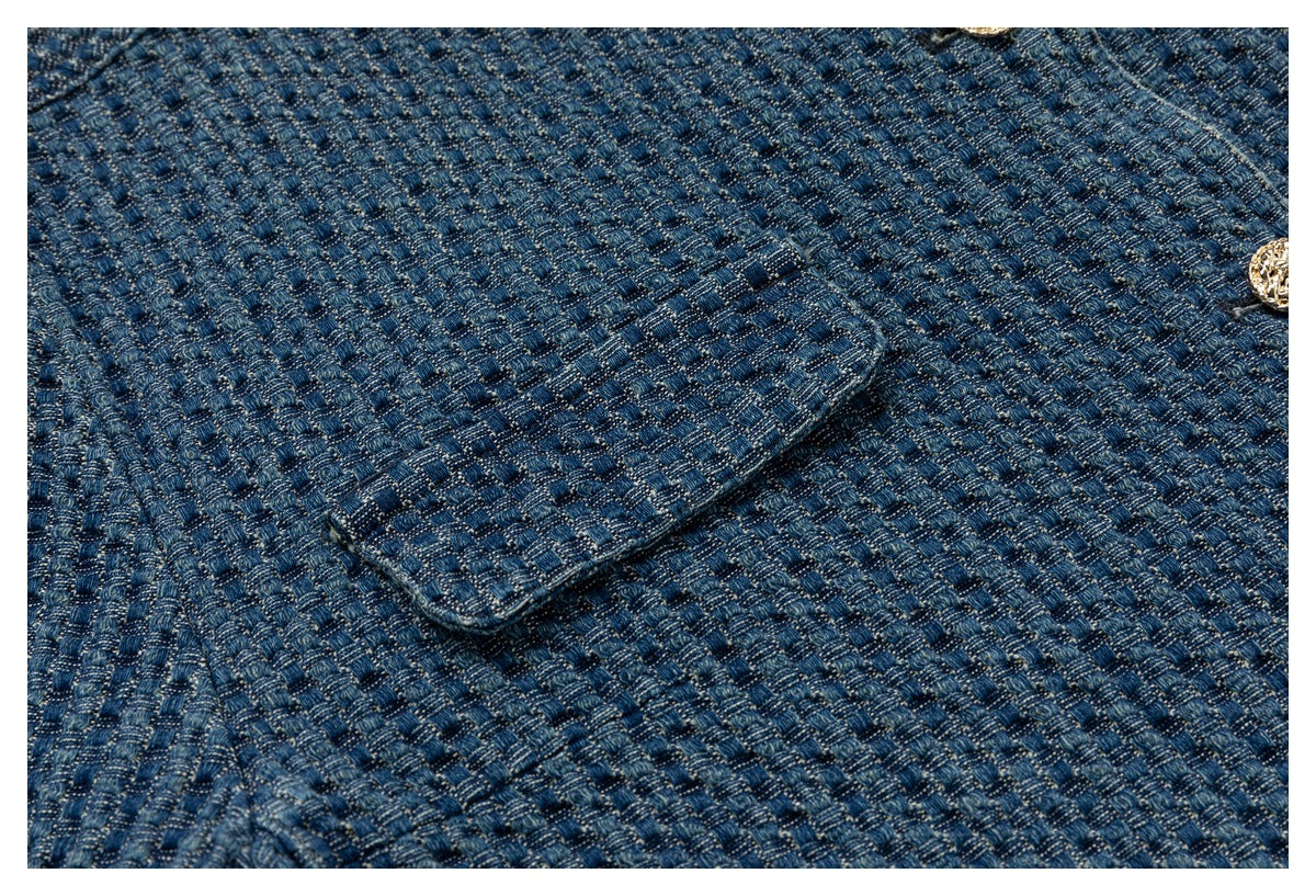 Close-up of blue textured woven fabric with a flap pocket and partial gold-tone button.